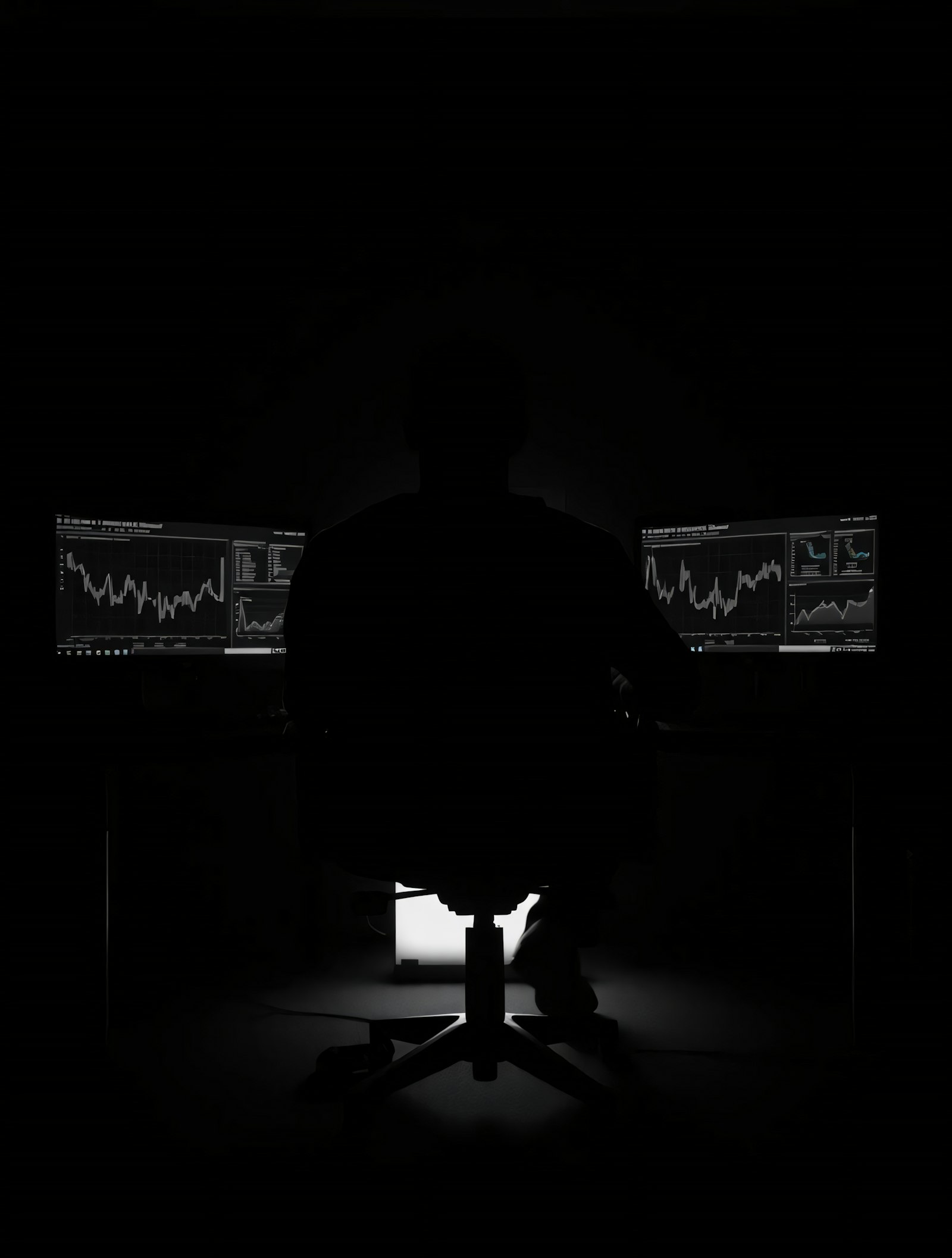 An analyst silhouetted against dashboards in a dark room