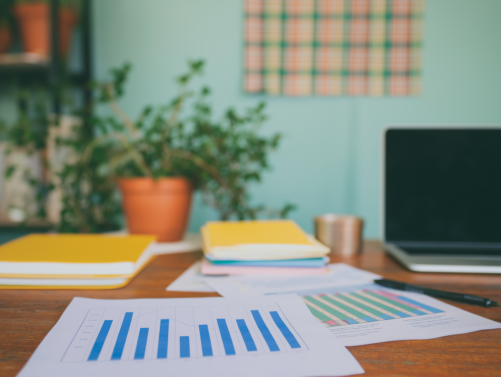 A desk with printed charts, notebooks, and a plant