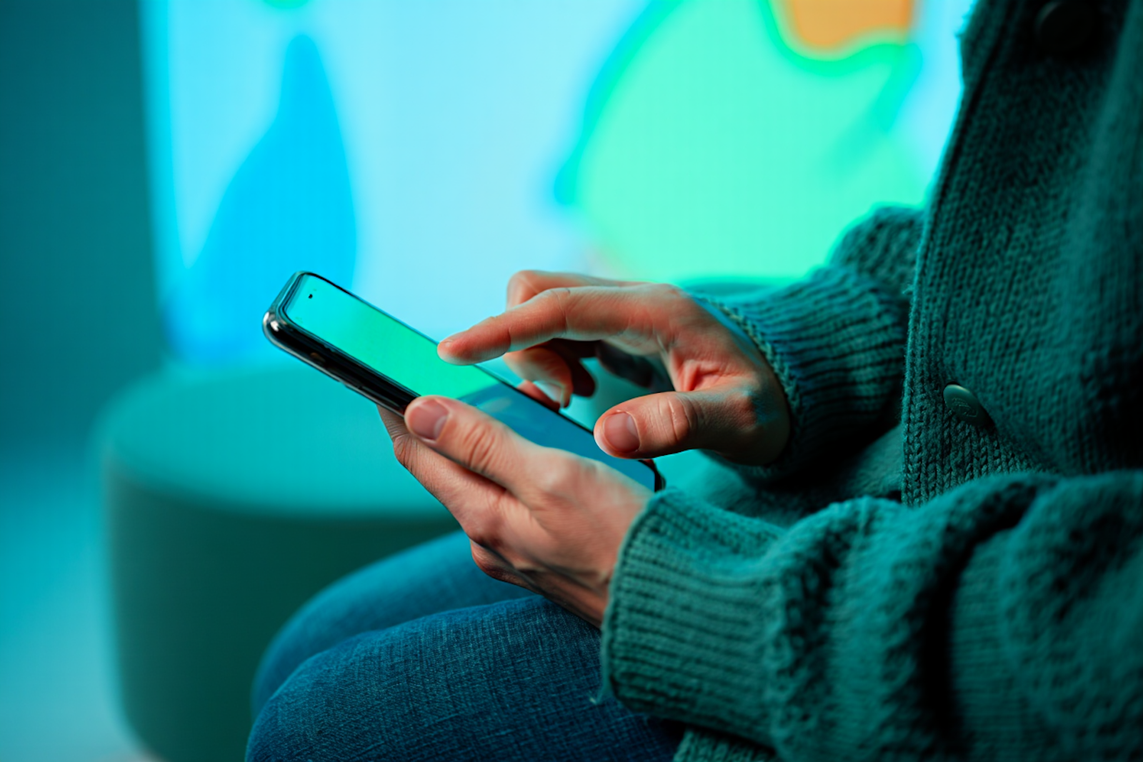 Hands in a green sweater holding a smartphone