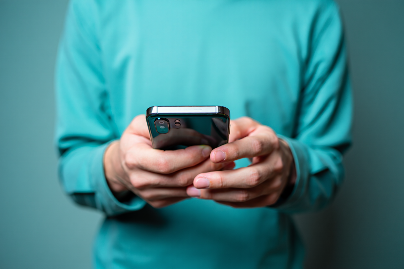 A person in a teal shirt holding a phone