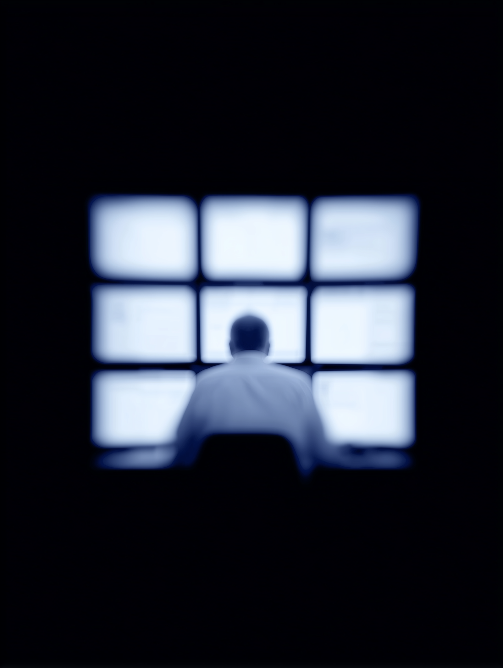 A person seated before a wall of glowing monitors